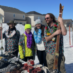 four people holding skis looking like staff or volunteers, two are wearing hawaiian shirts