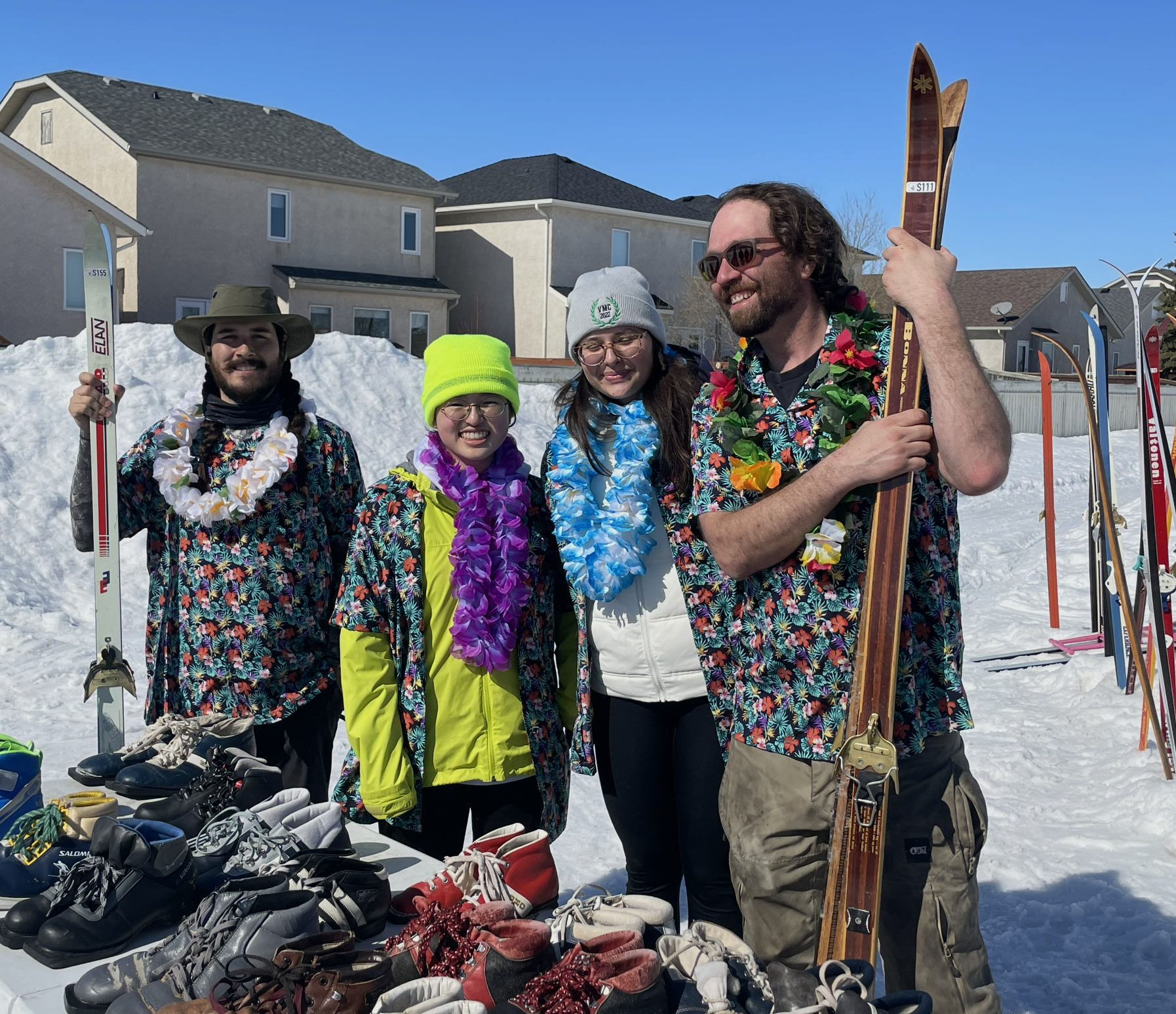 four people holding skis looking like staff or volunteers, two are wearing hawaiian shirts