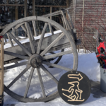 A weathered wooden horsedrawn cart in front of a glass window flanked by ski equipment