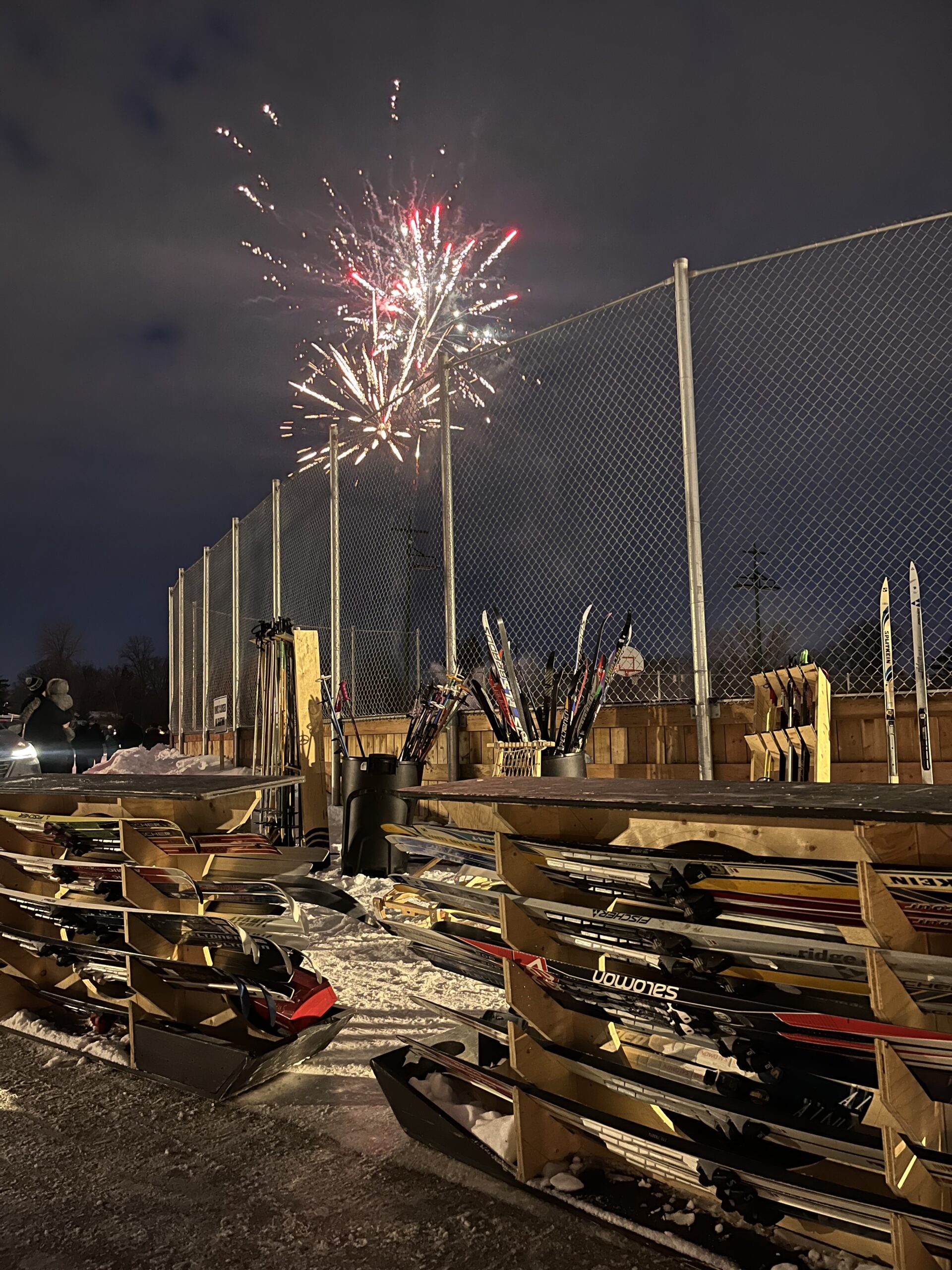 A rack full of skis with fireworks in the background.
