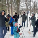 A large group of people standing in a circle with skis smiling