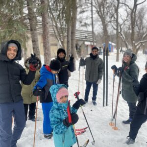 A large group of people standing in a circle with skis smiling