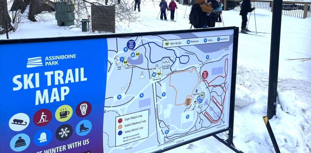 A large ski trail map of Assiniboine park in the foreground with people skiing oin the bachground.
