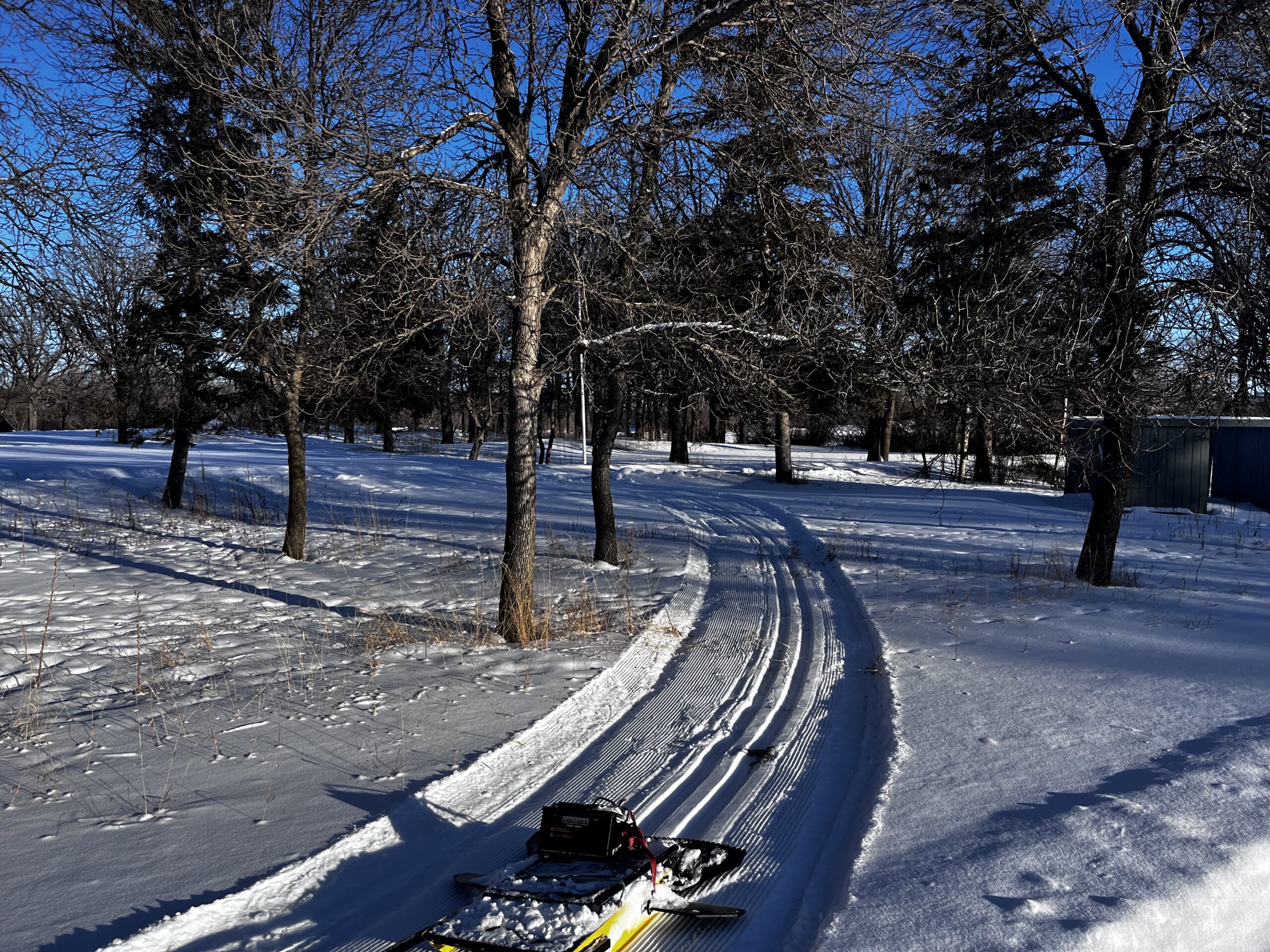 An yellow ski trail track setter in front of a curving ski trail