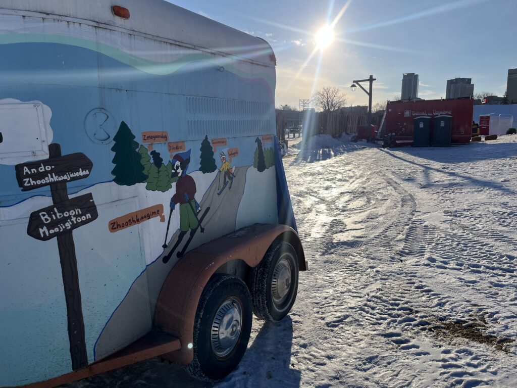 A trailer with a painted mural of cartoon animals doing winter activities in front of a "Boite a chansons" music trailer on a winter day